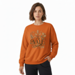 Woman wearing a VALE graphic cotton sweatshirt with autumn leaf botanical design, available in Beige, Slate Blue, and Burnt Orange.