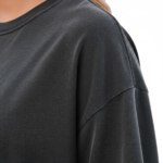 Rear and front view of a woman wearing an oversized breathable cotton t-shirt in charcoal, beige, and brown. The back features a colorful retro graphic of mushrooms and daisies with the text "Love Yourself." The front features a small white minimalist logo on the left chest.