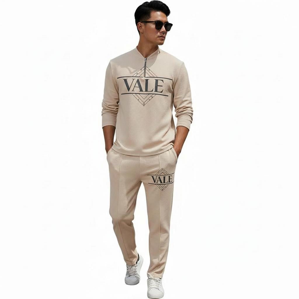 A professional male model wearing a VALE minimalist cotton tracksuit featuring a quarter-zip sweatshirt and matching joggers, isolated on a white background.