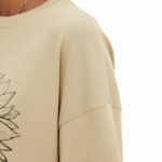 Front view of a woman wearing a Vale brand oversized cotton t-shirt featuring a large black line-art sunflower graphic, available in beige, blue, and green.
