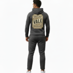 Man wearing a textured breathable cotton tracksuit with a vintage traveler's badge on the back, available in Obsidian Navy, Forest Green, and Heather Charcoal.