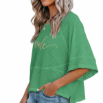 Woman wearing a breathable cotton oversized "Vale" t-shirt with gold script lettering and horizontal seam detail, available in green, blue, and red.
