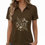 Female model wearing a slim-fit breathable cotton pique polo shirt featuring a "VALE" botanical graphic with ferns, flowers, and a dragonfly. Available in Forest Green, Charcoal Grey, and Earthy Brown.