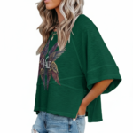 : A person wearing an oversized breathable cotton shirt featuring a "VALE" logo with colorful layered angel wings on the front, available in green, black, and purple.