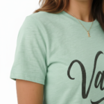Woman wearing a "Vale" script graphic t-shirt made of breathable cotton, paired with distressed denim jeans, available in Slate Blue, Heather Grey, and Mint Green.