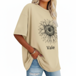 Front view of a woman wearing a Vale brand oversized cotton t-shirt featuring a large black line-art sunflower graphic, available in beige, blue, and green.