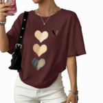 Front view of a woman wearing an oversized breathable cotton t-shirt with a triple heart graphic design and a small "V" logo, styled with white denim shorts and a black shoulder bag.