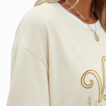 Woman wearing VALE graphic cotton t-shirt with striped sleeves and laurel wreath design in Blue, Plum, and Cream colors.