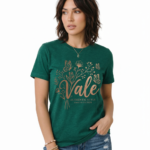Woman wearing a Vale Authentic Style limited edition graphic t-shirt featuring rose gold butterfly and floral art on forest green, white, and burgundy cotton fabric.