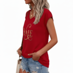 Professional studio shot of a woman wearing a VALE brand V-neck breathable cotton t-shirt with a metallic gold cursive logo, styled with denim jeans and gold accessories.