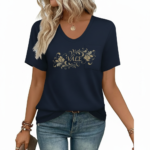 Close-up of a woman wearing a breathable cotton V-neck t-shirt featuring a gold floral "VALE" graphic and a small chest pocket, paired with blue jeans.