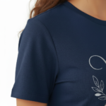 A female model showcasing the VALE branded floral graphic t-shirt in Navy Blue, Black, and White. 100% breathable cotton fabric featuring a silver script logo and elegant floral wreath design on a clean white background.
