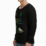 A man wearing a long-sleeve cotton shirt with a "VALE" nature graphic featuring a mountain, eagle, and tree, available in cream, black, and chocolate brown.