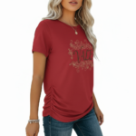 A woman wearing a slim-fit cotton graphic t-shirt featuring the word "VALE" inside a floral wreath design. Available in Dusty Blue, Olive Green, and Deep Maroon colors.