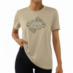 A woman wearing a premium breathable cotton t-shirt featuring the "Vale" brand logo in white script surrounded by a floral wreath with pink roses. Available in forest green, mustard orange, and cream beige colors.