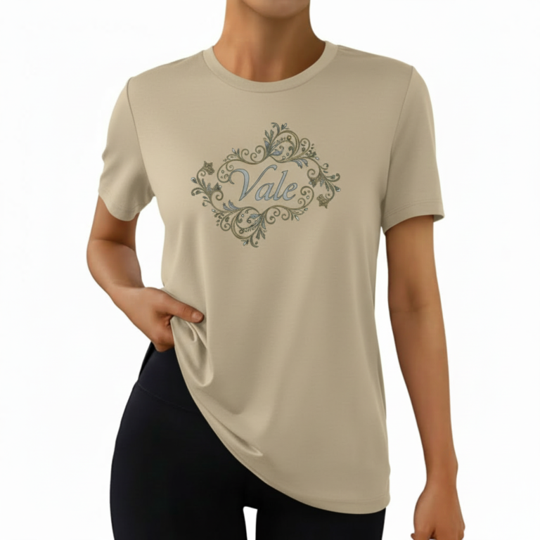 A woman wearing a premium breathable cotton t-shirt featuring the "Vale" brand logo in white script surrounded by a floral wreath with pink roses. Available in forest green, mustard orange, and cream beige colors.
