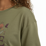Young woman wearing a "Vale Girl" breathable cotton t-shirt with a vintage floral and hummingbird graphic design, available in Olive Green, Royal Blue, and Red.