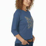 A woman wearing a VALE brand 3/4 sleeve raglan shirt made of breathable cotton, featuring a large, ornate butterfly embroidery on the chest in gold and light blue.