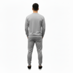 Full-body studio mockup of a man wearing a VALE brand breathable cotton tracksuit featuring a hand-passing-a-key graphic and ink-splatter design, available in grey, brown, and white-black contrast.