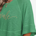 Woman wearing a breathable cotton oversized "Vale" t-shirt with gold script lettering and horizontal seam detail, available in green, blue, and red.