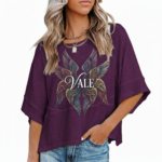 : A person wearing an oversized breathable cotton shirt featuring a "VALE" logo with colorful layered angel wings on the front, available in green, black, and purple.
