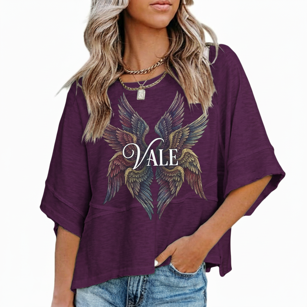 : A person wearing an oversized breathable cotton shirt featuring a "VALE" logo with colorful layered angel wings on the front, available in green, black, and purple.