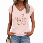 Professional studio shot of a woman wearing a VALE brand V-neck breathable cotton t-shirt with a metallic gold cursive logo, styled with denim jeans and gold accessories.