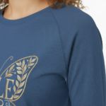 A woman wearing a VALE brand 3/4 sleeve raglan shirt made of breathable cotton, featuring a large, ornate butterfly embroidery on the chest in gold and light blue.