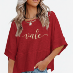 Woman wearing a breathable cotton oversized "Vale" t-shirt with gold script lettering and horizontal seam detail, available in green, blue, and red.
