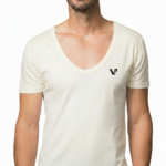 Close-up of a model wearing a premium men's deep V-neck cotton t-shirt in cream with a small black embroidered V-logo on the left chest.