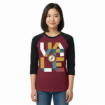 A woman wearing a breathable cotton raglan baseball shirt featuring a colorful geometric "VALE" logo and a central compass graphic. Available in Maroon, Grey, and Olive Green sleeves with a black or burgundy torso.