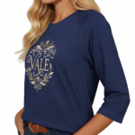 Woman wearing a breathable cotton 3/4 sleeve raglan shirt featuring a gold-toned floral "VALE" crest design, available in Navy Blue, Earthy Brown, and Maroon.