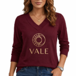 Front view of a woman wearing a VALE brand long sleeve V-neck cotton shirt featuring a gold celestial sun and moon logo, available in maroon, brown, and orange.