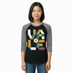 A woman wearing a breathable cotton raglan baseball shirt featuring a colorful geometric "VALE" logo and a central compass graphic. Available in Maroon, Grey, and Olive Green sleeves with a black or burgundy torso.