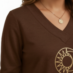 Front view of a woman wearing a VALE brand long sleeve V-neck cotton shirt featuring a gold celestial sun and moon logo, available in maroon, brown, and orange.