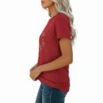 A woman wearing a slim-fit cotton graphic t-shirt featuring the word "VALE" inside a floral wreath design. Available in Dusty Blue, Olive Green, and Deep Maroon colors.