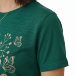 Woman wearing a Vale Authentic Style limited edition graphic t-shirt featuring rose gold butterfly and floral art on forest green, white, and burgundy cotton fabric.