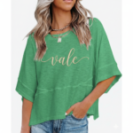 Woman wearing a breathable cotton oversized "Vale" t-shirt with gold script lettering and horizontal seam detail, available in green, blue, and red.