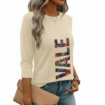 A woman wearing a breathable 3/4 sleeve cotton t-shirt with a colorful vertical "VALE" graphic print, available in cream, red, and black