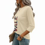 A woman wearing a breathable 3/4 sleeve cotton t-shirt with a colorful vertical "VALE" graphic print, available in cream, red, and black