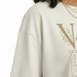 A woman modeling an oversized VALE brand t-shirt featuring a vintage-style Protea flower graphic and celestial symbols. Available in black, grey, and cream colors.