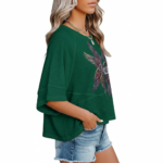 : A person wearing an oversized breathable cotton shirt featuring a "VALE" logo with colorful layered angel wings on the front, available in green, black, and purple.