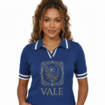 A high-quality studio shot of a model wearing a VALE brand breathable cotton polo shirt featuring white-tipped collars and a detailed gold floral celestial embroidery on the chest.