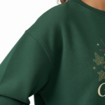 Woman wearing a VALE graphic cotton sweatshirt featuring a swallow, butterfly, and botanical nature design in Forest Green, Black, and Purple colors.