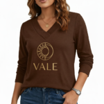 Front view of a woman wearing a VALE brand long sleeve V-neck cotton shirt featuring a gold celestial sun and moon logo, available in maroon, brown, and orange.