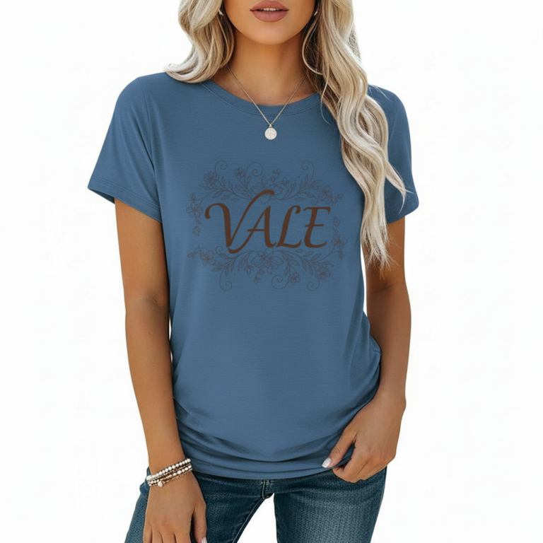 A woman wearing a slim-fit cotton graphic t-shirt featuring the word "VALE" inside a floral wreath design. Available in Dusty Blue, Olive Green, and Deep Maroon colors.