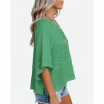 Woman wearing a breathable cotton oversized "Vale" t-shirt with gold script lettering and horizontal seam detail, available in green, blue, and red.