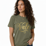 Woman wearing a breathable cotton t-shirt with "Vale" gold script calligraphy design, available in brown, olive green, and maroon.