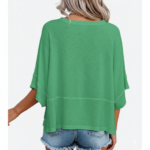 Woman wearing a breathable cotton oversized "Vale" t-shirt with gold script lettering and horizontal seam detail, available in green, blue, and red.