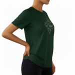 A woman wearing a premium breathable cotton t-shirt featuring the "Vale" brand logo in white script surrounded by a floral wreath with pink roses. Available in forest green, mustard orange, and cream beige colors.